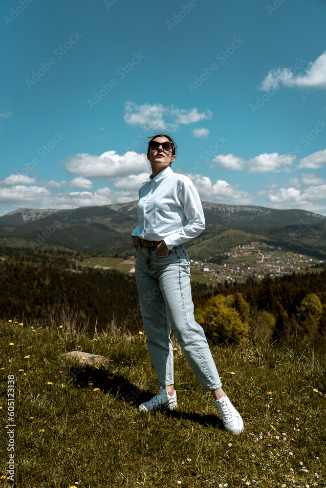 Stylish woman in a white shirt and glasses posing against the backdrop of mountains