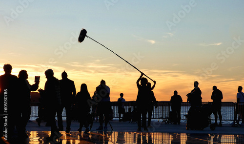 silhouette of people recording movie with sound recorder man holding boom microphone against dusk sky in Zadar, Croatia