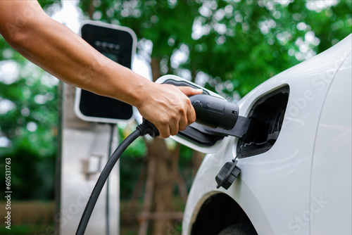 Фотография Hand inserting EV charging plug to electric vehicle in focus shot with blurred background of outdoor natural greenery