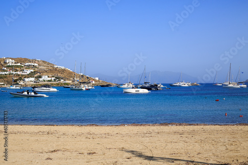 Ornos in Mykonos, Greece is a small coastal town with lots of small coves, luxury boats and yachts are moored on the bright blue calm sea.