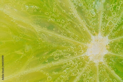 Slice of ripe lime in water. Close-up of lime in liquid with bubbles. Slice of ripe lime in sparkling water. Macro horizontal image of fruit in carbonated water.