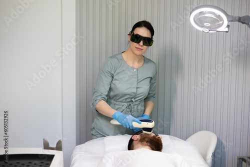 Laser depilation of beard contour. Man getting permanent laser face hair removal at beauty salon, beauty unpainful procedure treatment. Doctor in protective eyewear looking at camera portrait. photo