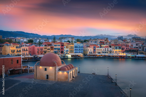 Captivating sunset over Chania's harbor & old city in Crete, Greece; a stunning blend of colors illuminates the skyline, creating a picturesque coastal scene.
