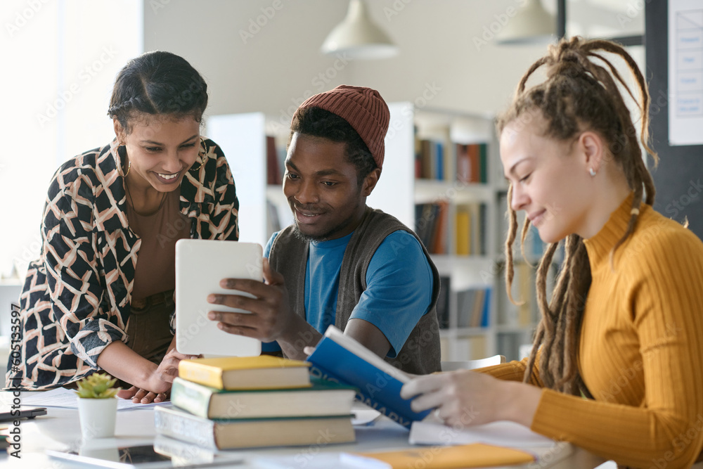 Multiethnic students watching video on digital tablet while doing homework together sitting in the library Multiethnic students watching video on digital tablet while doing homework together sitting in the library