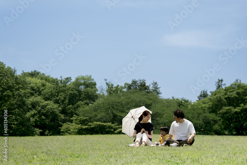 Family relaxing on park lawn with mother under parasol Relaxing on leisure seat Copy space available Wide angle © kapinon
