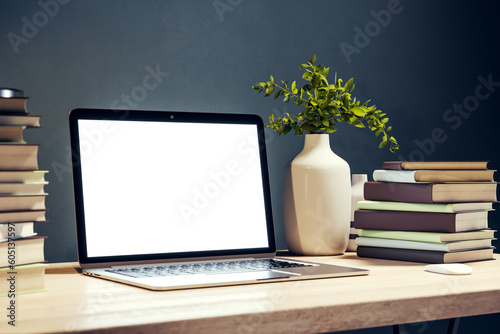 Side view of student wooden desk with white screen laptop and a lot of books on black wall background in modern cozy interior with lamp and plant, mockup. Education and learning concept. 3D Rendering