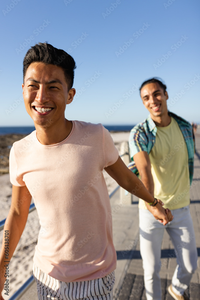 Happy biracial gay male couple holding hands on sunny promenade by the sea Happy biracial gay male couple holding hands on sunny promenade by the sea