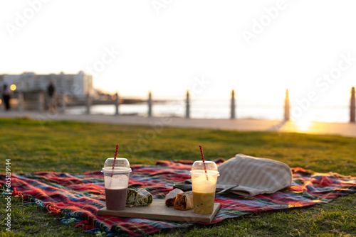 Close up of blanket with drinks and food on promenade by sea at sundown, with copy space