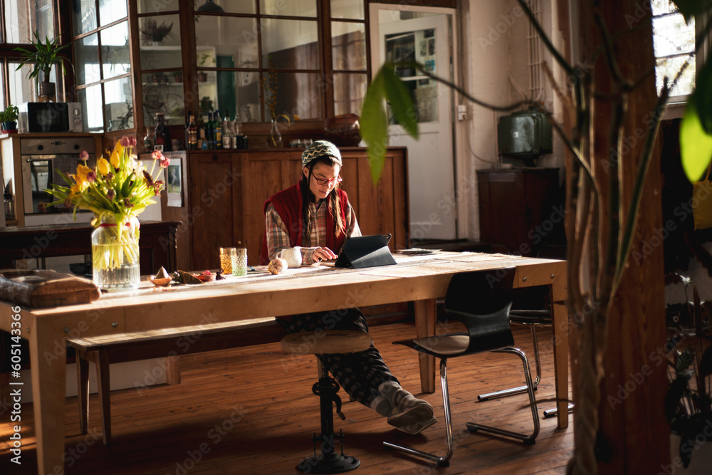 © Cavan Images - person sits at home office with flowers working on ipad in sunlight © Cavan Images - person sits at home office with flowers working on ipad in sunlight