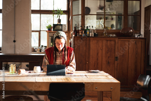 Asian woman works on ipad device at home on wooden table in sun photo