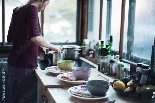 woman in light kitchen at home prepares meal with bowls and pots photo