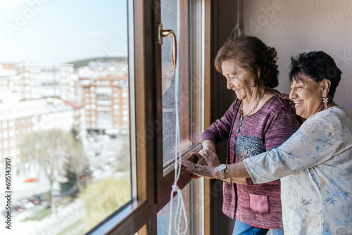 two elderly female friends looking out the window of their house photo