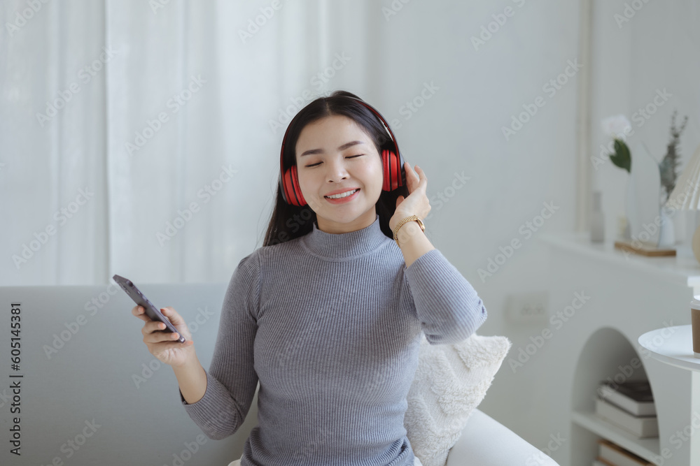 Asian woman dancing to the music playing from laptop on sofa in her home living room, weekend break, relaxation from hard work, drinking coffee. Take a vacation after a hard day's work. Asian woman dancing to the music playing from laptop on sofa in her home living room, weekend break, relaxation from hard work, drinking coffee. Take a vacation after a hard day's work.