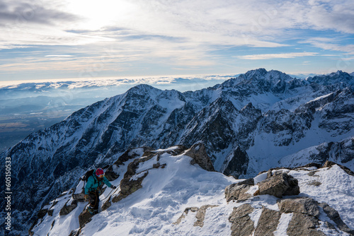 Adventurous women hiker on top of a steep rocky cliff overlooking winter alpine like moutain landscape of High Tatras, Slovakia. Alpine mountain landscape covered with glaciers, snow and ice.
