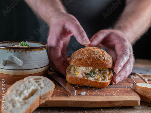 Man is holding a sandwich with tuna salad on a german bun