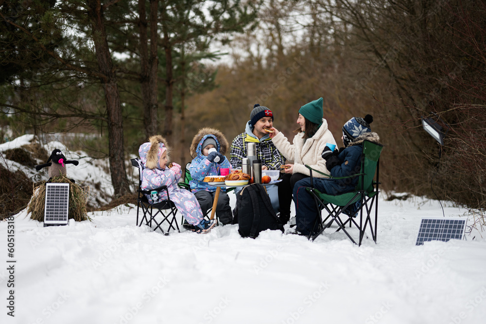 Family with three children in winter forest spending time together on a picnic.