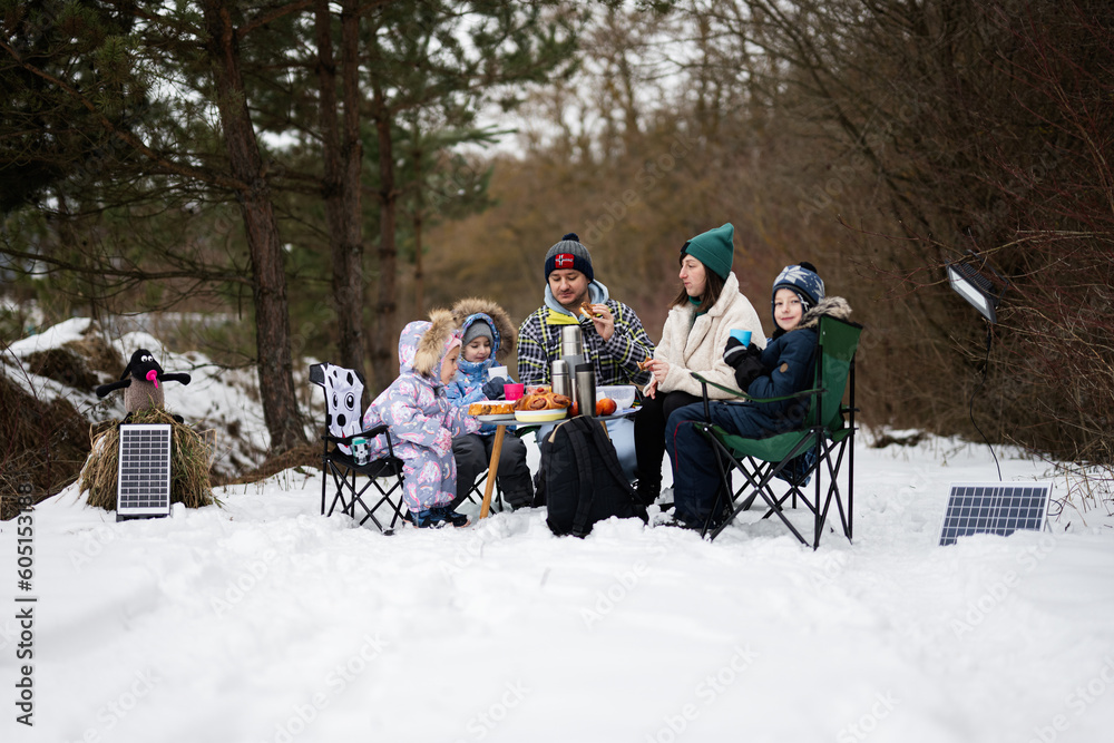 Family with three children in winter forest spending time together on a picnic.