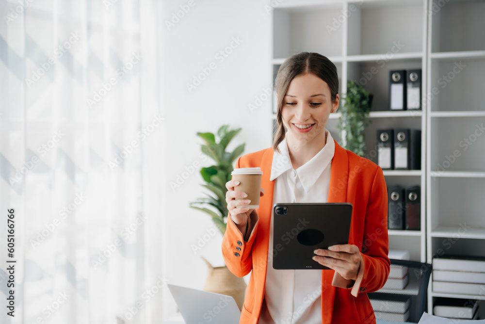 Confident business expert attractive smiling young woman typing laptop ang holding digital tablet on desk in creative office.. Confident business expert attractive smiling young woman typing laptop ang holding digital tablet on desk in creative office..