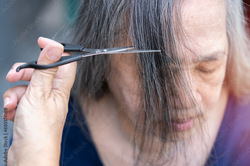 Obraz premium Hands of a young hairdresser cutting the hair of an old Asian lady. Lifestyle.