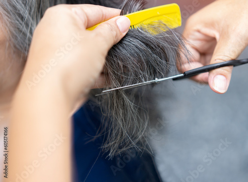 Cropped image of hands working with hair scissors. Professional hairstyler woman cutting hair of mature woman. photo