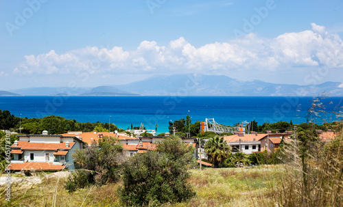 View of the Aegean town in Turkey, blue sea, white clouds on the sky, grass and houses 