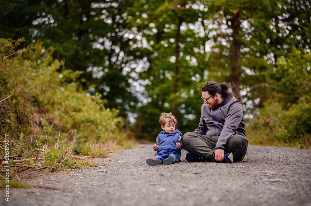 Young long hair bearded man in glasses sitting with little toddler boy on road playing with stones