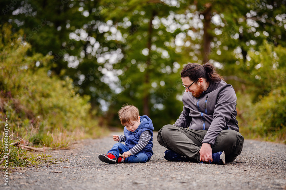 Young long hair bearded man in glasses sitting with little toddler boy on road playing with stones