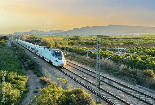 Train on railway on sunset in mountain. Speed train in motion on Valencia railroad. European passenger train on railway. High-speed train. Spanish National Rail Network. photo