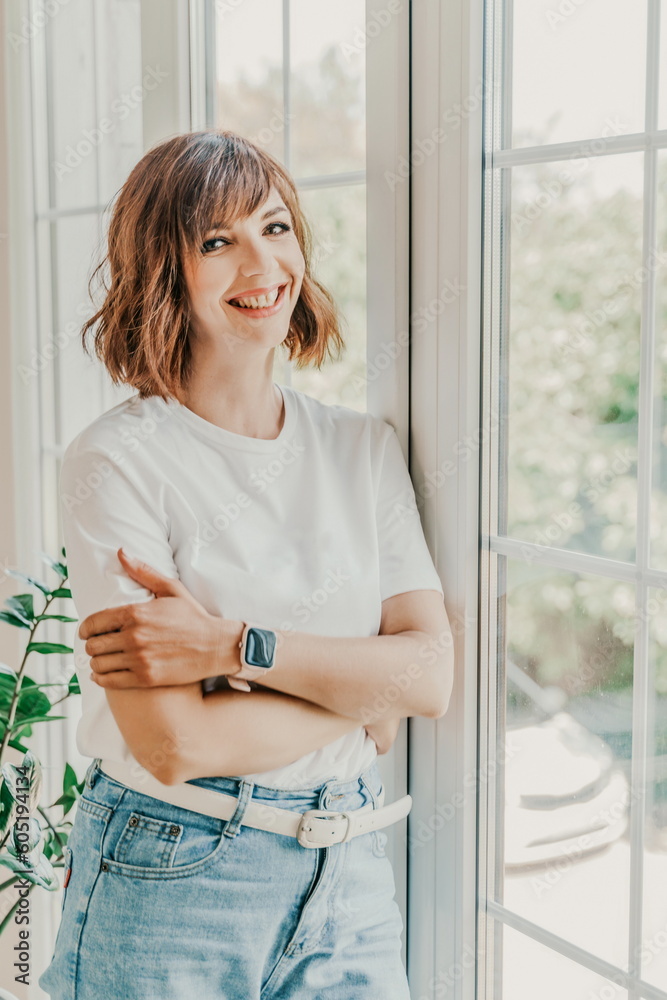 Office window woman. Business woman standing in the office with her arms crossed near the window. Dressed in a white T-shirt and jeans. Office window woman. Business woman standing in the office with her arms crossed near the window. Dressed in a white T-shirt and jeans.