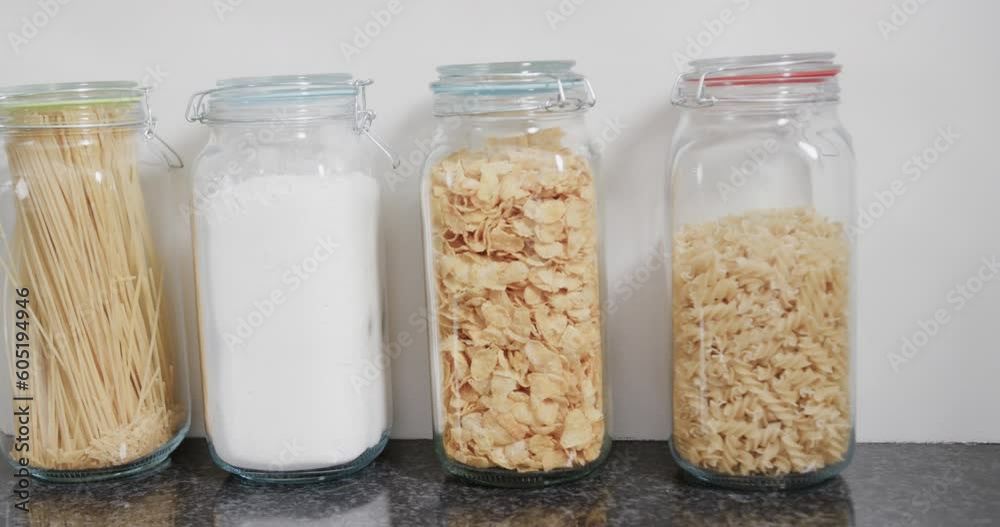Close up of food storage jars with flour and various kinds of pasta on shelf in kitchen, slow motion Close up of food storage jars with flour and various kinds of pasta on shelf in kitchen, slow motion
