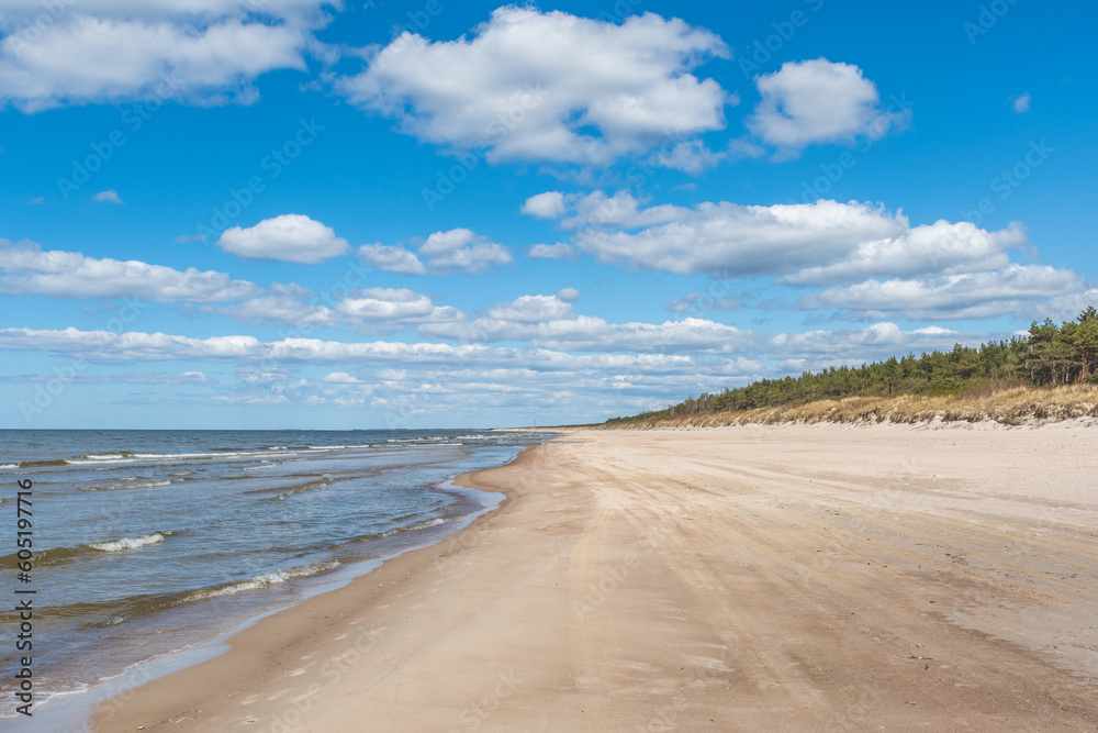 Walking on the Baltic Sea in Palanga, Klaipeda, Lithuania, with waves, cloudy sky, white sandy beach and dunes with reeds and pine tree forest