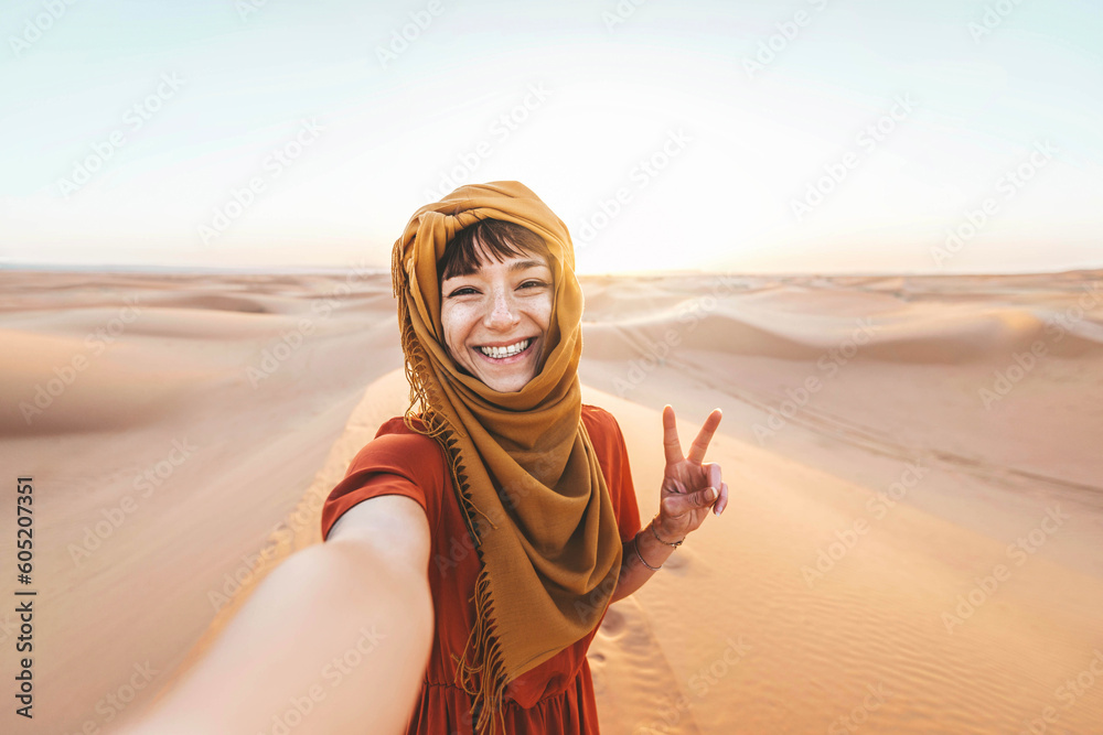Happy female tourist taking selfie on sand dunes in the Africa desert, Sahara National Park - Influencer travel blogger enjoying trip while takes self portrait - Summer vacation and weekend activities - obrazy, fototapety, plakaty 