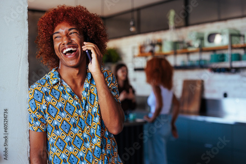 Young African-American man laughing during phone call while two women talk in the background.