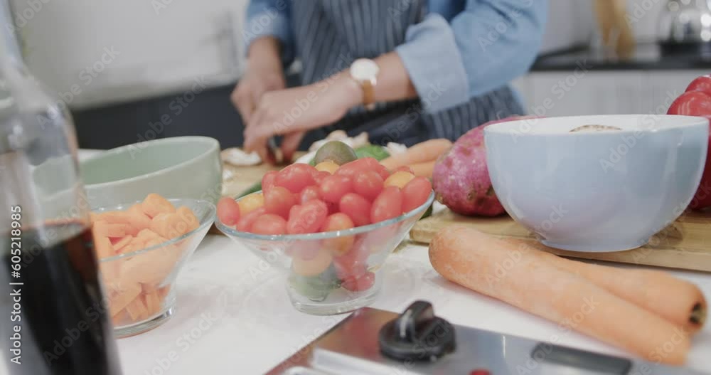 Midsection of biracial woman in apron preparing meal, chopping vegetables in kitchen, slow motion Midsection of biracial woman in apron preparing meal, chopping vegetables in kitchen, slow motion