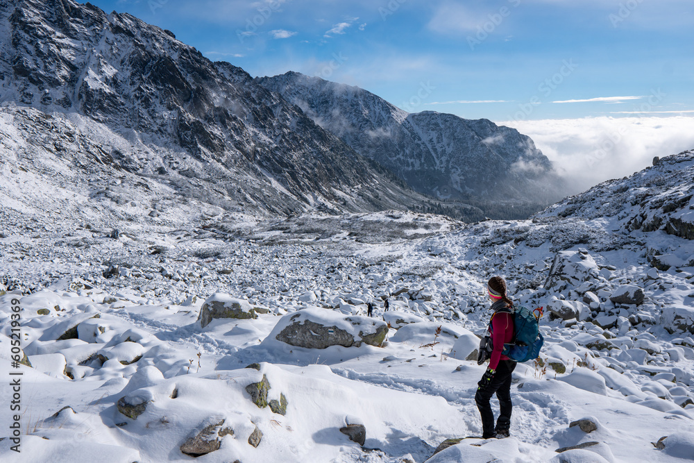 Hiker woman standing and looks around, admiring winter mountain landscape. Happy tourist woman in winter. High Tatras, 1987 meter above sea level. Slovakia - obrazy, fototapety, plakaty 