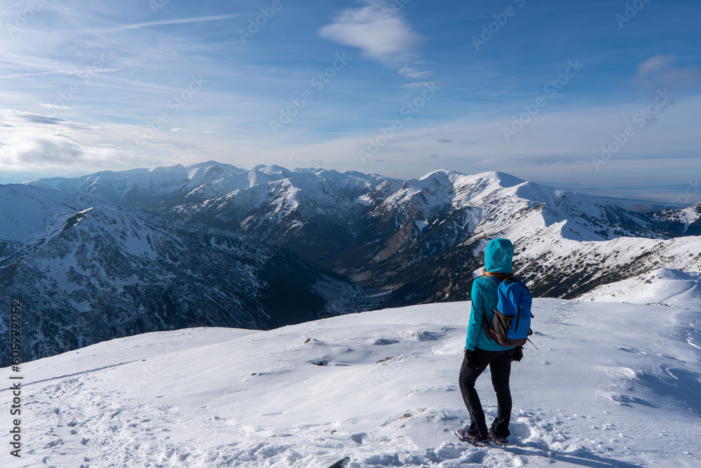 Hiker woman standing and looks around, admiring winter mountain landscape. Happy tourist woman in winter. High Tatras, 1987 meter above sea level. Slovakia - obrazy, fototapety, plakaty 
