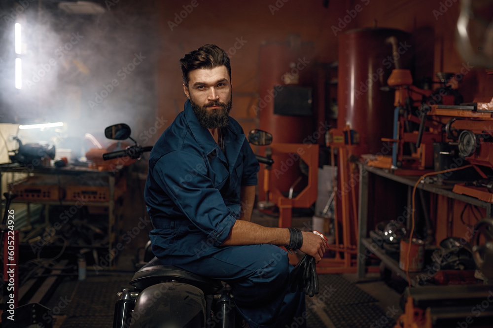 Portrait of tired but happy workman sitting on repaired motorcycle in workshop Portrait of tired but happy workman sitting on repaired motorcycle in workshop