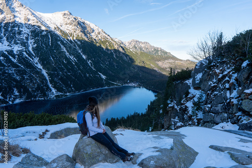 Tourist woman near the mountain lake Morskie Oko in Tatra National Park, Poland. Young happy hiker woman rising hands on the picturesque lake in the mountains in summer. 