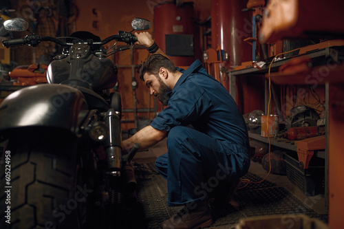 Mechanic working with motorcycle engine in workshop while sitting nearby vehicle