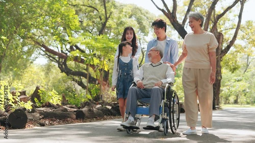 Happy Asian senior man sitting on wheelchair in the public park with big family on weekends holiday
