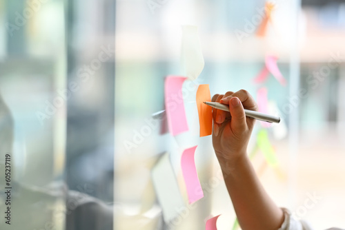 Select focus on hand of female employee writing tasks, new ideas planning corporate strategy creation on sticky notes in office photo