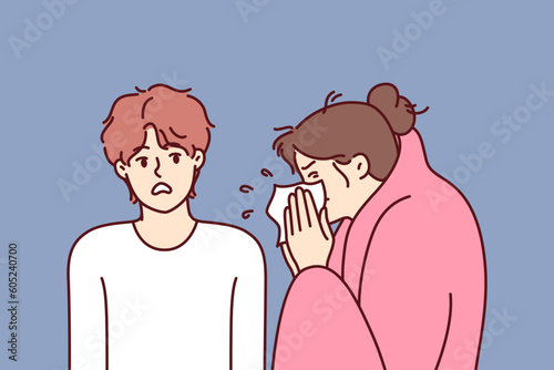 Sick woman sneezes standing near guy afraid of contracting dangerous flu or cold. Sick girl with handkerchief is wrapped in blanket and needs treatment and antibiotics to fight infection.