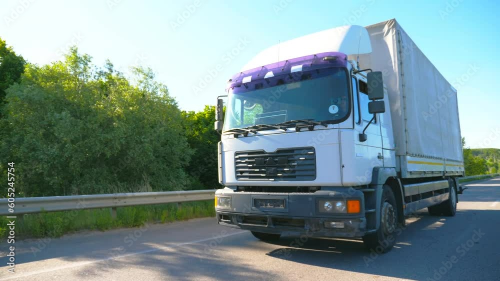 Big truck with cargo trailer driving on highway and transporting goods at sunny day. White lorry riding to destination through countryside road. Beautiful background. Slow motion Front view Close up Big truck with cargo trailer driving on highway and transporting goods at sunny day. White lorry riding to destination through countryside road. Beautiful background. Slow motion Front view Close up