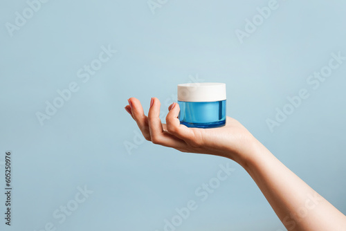 Woman holding a blue glass jar of skin cream on blue background. Skin care concept. Moisturizing cream in female hand . Beauty treatment. Copy space