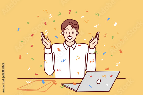 Happy man office worker with laptop raises hands up as sign of success and sits among falling confetti. Happy business man enjoying moment after making successful deal with partners