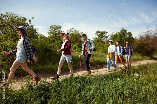 Young people, group of friends walking in forest on path, going hiking on warm summer day. Tourism and leisure time. Concept of active lifestyle, nature, sport and hobby, friendship, fun photo