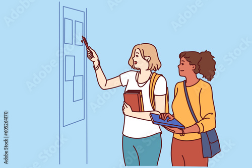 Girls students stand in corridor of college or university near blackboard with lesson schedule or lists of pupils. Two schoolgirls or students with books in their hands read notice on bulletin board