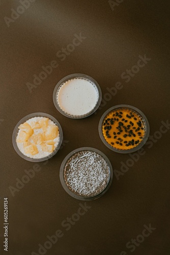 Vertical shot of plastic bowls of various creamy pudding on a brown surface © Camila Silva Cordeiro1/Wirestock Creators