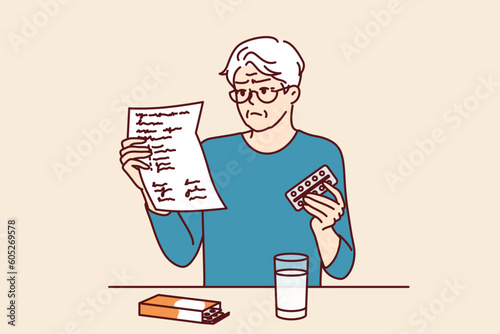 Elderly man takes medicine and reads dosage instructions for pills prescribed by doctor. Gray-haired elderly human is studying instructions to learn about contraindications and side effects of pills.