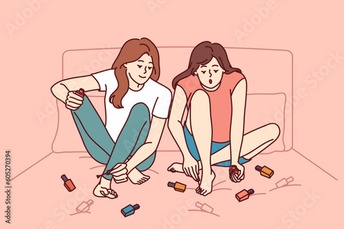 Two girls paint nails sitting on bed and doing pedicure before going to beach or party. Women friends paint toenails with varnish of different colors, wanting to be beautiful and elegant.